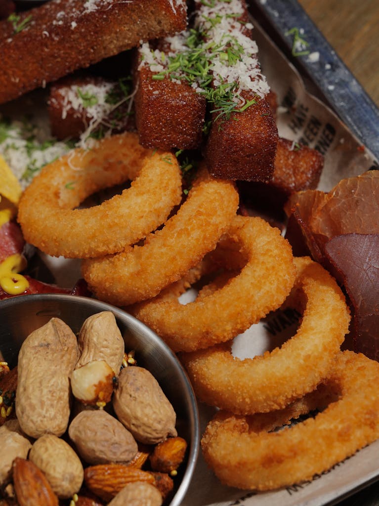 Delicious assortment of fried snacks including onion rings, breaded bites, and nuts on a tray.